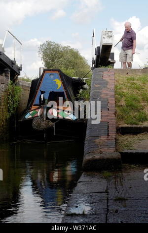 Un proprietario della barca del canale che tira la sua barca stretta con la corda tramite un blocco dopo aver abbassato il livello dell'acqua sul Grand Union Canal vicino Aylesbury Foto Stock