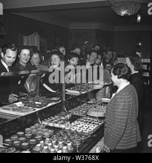 1940s:00 caffetteria e fika time. Due donne sono in piedi dietro il bancone che è pieno di torte e dolci appena sfornati. Una folla di persone è in linea con l'ordine. Svezia 1943 Kristoffersson Rif. E126-2 Foto Stock