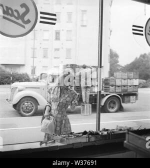 Window shopping negli anni cinquanta. La giovane attrice Erna Groth, 1931-1993, raffigurato al di fuori di un negozio di alimentari finestra dove ella punti con il suo dito per scegliere le verdure nella vetrina di un negozio. Sullo sfondo di una consegna carrello con casse di birra e di altre bevande per la distribuzione. La Svezia 1952. Kristoffersson BG68-3 Foto Stock