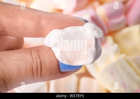 Una mano che stringe un morbido marshmallow, oltre colorato sfondo marshmallows Foto Stock