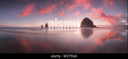 Il tramonto a Cannon Beach con spettacolari nuvole sullo sfondo e un bel riflesso in acqua. Spettacolare paesaggio costiero con rocce panoramiche Foto Stock