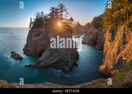 Tramonto al Samuel H. Boardman state Scenic Corridor, Oregon, durante un tramonto d'ora d'oro - raggi del sole attraverso gli alberi con fitta vegetazione. Bel mare Foto Stock