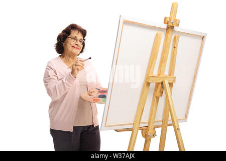 Felice donna anziana con una spazzola e vernici pittura su una tela di canapa isolati su sfondo bianco Foto Stock