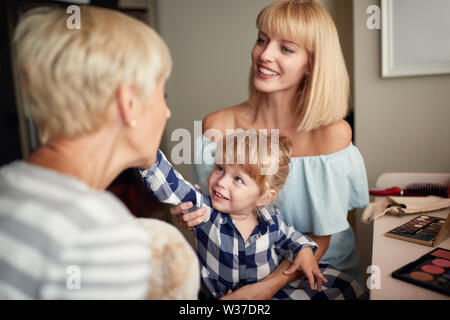Poco carino mettendo ragazza trucco sulla faccia a sua nonna Foto Stock