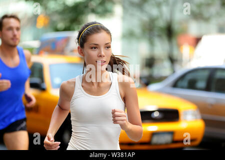 Le persone attive jogging sulla città di New York Street, New York. Giovani asiatici runner donna e uomo caucasico in esecuzione insieme alla formazione di Manhattan il traffico intenso con giallo taxi in estate. Foto Stock
