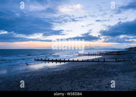 Nuvole temporalesche al crepuscolo sulla spiaggia panoramica con waterbreak in legno. Blaenau Ffestiniog in Galles, Regno Unito Foto Stock