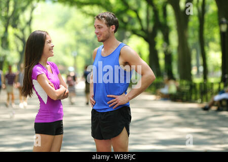 Felice coppia guide a parlare dopo aver eseguito nel parco di NYC. Femmina e maschio adulto atleti in appoggio insieme a Central Park di New York City, indossando active top e shorts abbigliamento sportivo per un allenamento estivo. Foto Stock