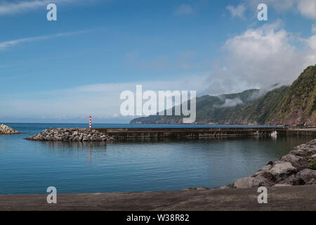 Parete di separazione tra oceano Atlantico dalla zona di un piccolo porto. Montagne sullo sfondo. Il cielo blu con nuvole bianche. Povoacao, Sao Miguel, Azzorre è Foto Stock