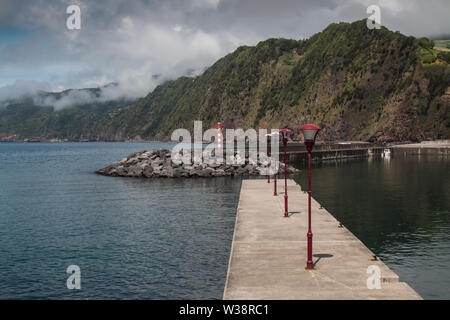 Parete di separazione tra oceano Atlantico dalla zona di un piccolo porto. Montagne sullo sfondo. Il cielo blu con nuvole bianche. Povoacao, Sao Miguel, Azzorre è Foto Stock