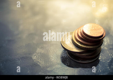 Una pila di lucido monete in euro su un tavolo di vetro con una calda luce del sole, selettivo soft focus Foto Stock