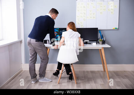 Vista posteriore di due imprenditori analizzando il grafico su schermo di computer in ufficio Foto Stock