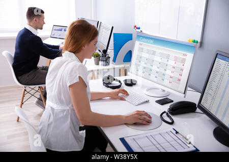 Imprenditrice guardando il Calendario sul computer desktop con il collega dietro in ufficio Foto Stock