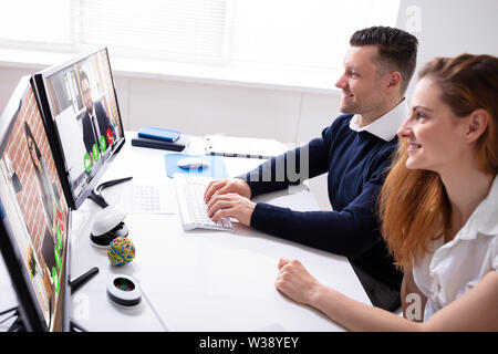 Vista laterale di imprenditrice e imprenditore, videoconferenze con i colleghi sul computer in ufficio Foto Stock