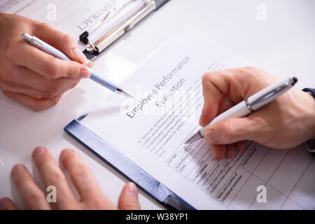 Close-up di una persona che riempie la valutazione delle prestazioni sotto forma di dipendente su scrivania Foto Stock