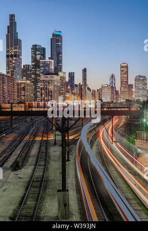 Treni pendolari si illuminano le tracce nei pressi di Soldier Field sotto la bellissima skyline del centro di Chicago, Illinois, su una chiara notte d'estate. Foto Stock