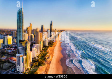 Waterfront dietro la spiaggia sabbiosa di Surfers paradise saluto Rising Sun oltre oceano Pacifico. Vista aerea lungo la Gold Coast e la linea di alti torri. Foto Stock