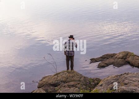 Maschio in piedi su una roccia vicino ad un mare che guarda giù Foto Stock