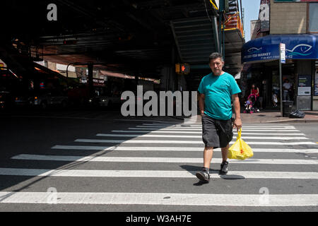 Un uomo di mezza età con una borsa da shopping attraversa la 96esima strada sotto l'elevata #7 treno a Roosevelt Ave in corona, Queens, a New York City. Foto Stock