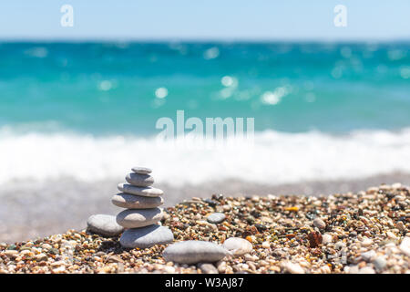Piramide di pietre. Obo da ciottoli. Torre di pietra sulla spiaggia contro il blu del mare. Equilibrio, pace della mente, pietre formano una piramide sulla spiaggia ghiaiosa Foto Stock
