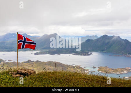 Norwegian bandiera nazionale rinuncia al vento sulla sommità del picco Nonstinden con fjord in background, Ballstad, Vestvagoy comune, Nordland cou Foto Stock