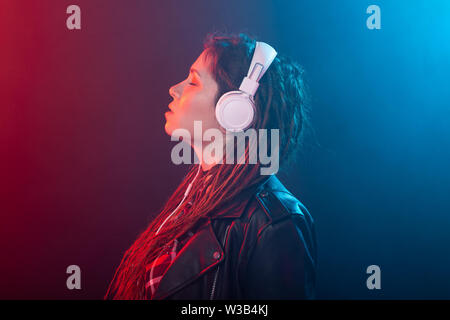 Godetevi, meloman e concetto di persone - una giovane donna con dreadlocks ascoltando la musica, ritratto su sfondo scuro Foto Stock