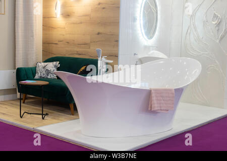 Bianco moderno design bagno con vasca da bagno e lavandino, asciugamano, divano, in legno per il rivestimento di pareti e pavimenti di colore viola. Foto Stock