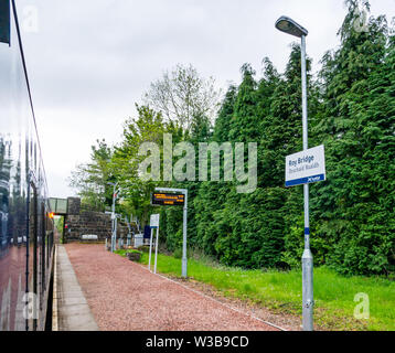 Roy Bridge rural stazione ferroviaria piattaforma e nome sign con treno ScotRail su West Highland linea ferroviaria, Highlands scozzesi, Scotland, Regno Unito Foto Stock