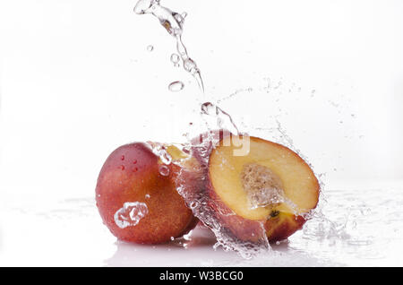 Un ondata di acqua chiara cade su alcune Nettarine Pesche su sfondo bianco Foto Stock