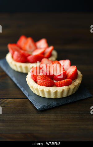 Tortine con crema pasticcera e fragole fresche servita su una piastra di ardesia. Dark tavolo in legno, ad alta risoluzione Foto Stock