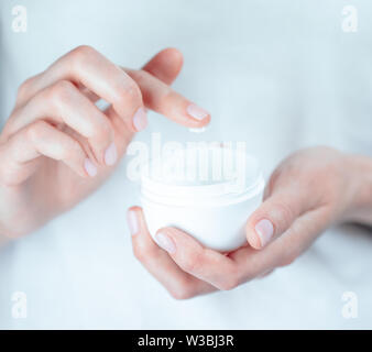 Donna tatuata mani tenendo un vasetto di crema. Dito con una goccia di crema bianca Foto Stock