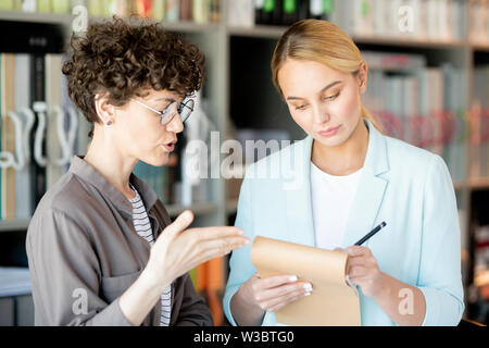 Uno dei colleghi che fanno le note o bozzetto mentre un'altra donna dare consigli Foto Stock