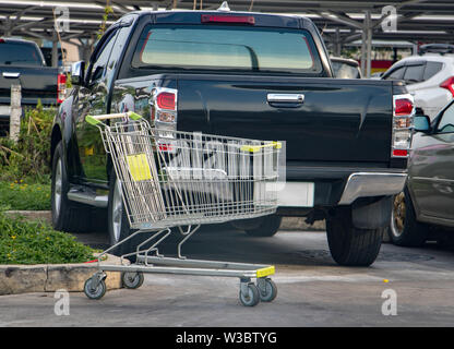 Un vuoto carrello sorge in un centro commerciale parcheggio con vetture a sfondo. Foto Stock