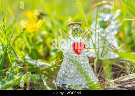 Due angeli con cuori rossi e verdi in mani si trovano tra l'erba luminosa del campo primaverile. Chiamata all'amore e alla cura della natura. Foto Stock
