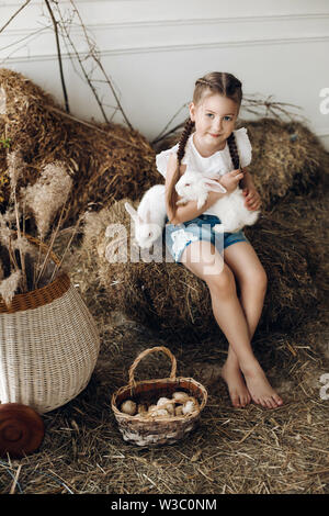 Adorabile bambina con trecce tenendo due adorabili e conigli. Foto Stock