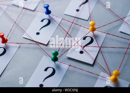 Rete di stampati punti interrogativi sulle carte bianche segnato con il pollice rampini e uniti da una stringa in una immagine concettuale su uno sfondo grigio Foto Stock