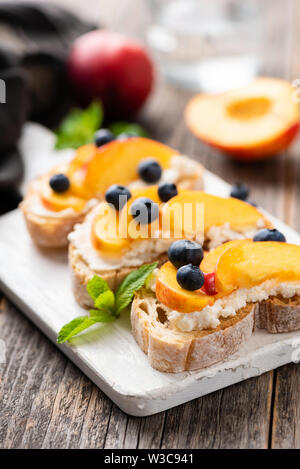 La bruschetta o antipasto toast con pesca, ricotta, mirtilli sulla tavola di legno. Messa a fuoco selettiva Foto Stock