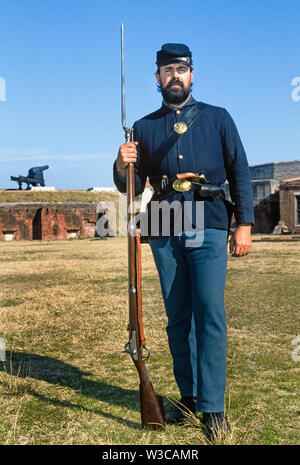 Un uomo barbuto che indossa la divisa militare di U.S. La guerra civile europea soldato pone con armi che egli porta come un interprete che accoglie i visitatori a Fort Clinch parco dello stato in Fernandina Beach sulla costa orientale della Florida, Stati Uniti d'America. La sua mano destra trattiene un Springfield rifled moschetto con il suo allegato a baionetta e una pistola è infilata nella cintura di cuoio intorno ai lombi che porta anche le munizioni. Questo storico fort all'entrata di Cumberland Sound e la Basilica di Santa Maria del fiume è stata inizialmente occupata dall'esercito confederato fino a quando passò sotto il controllo delle truppe dell'Unione nel 1862. Foto Stock