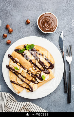 Crepes con salsa di cioccolato, banana e i dadi sulla piastra bianca. Tabella vista superiore dolce con il cibo