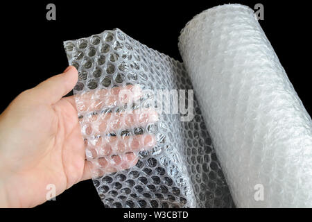Donna holdind mano un bianco trasparente Bubble wrap su uno sfondo nero. Materiale per l'imballaggio di oggetti fragili per un trasporto sicuro. Vista dall'alto. Foto Stock