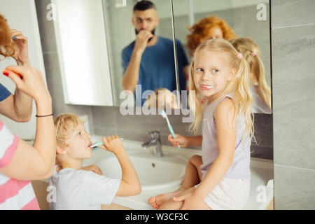 Sentirsi a proprio agio. Bella ragazza bionda seduta sul lavandino mentre spazzolare i suoi denti nella stanza da bagno Foto Stock