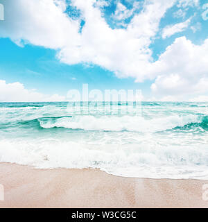 Le onde del mare crash sulla spiaggia sabbiosa. splendido clima soleggiato con nubi all'orizzonte. acqua color smeraldo sotto un cielo azzurro. La bellezza e la forza della natura con Foto Stock