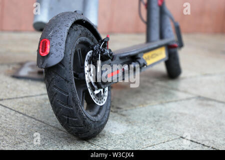 Lo scooter elettrico su un parcheggio durante una pioggia di gocce di acqua su una ruota. Tempo piovoso in una città, noleggio biciclette system Foto Stock