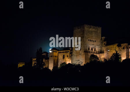 La vista sull'Alhambra con la luna, un castello moresco, fortezza e palazzo, illuminata di notte a Granada, Spagna Foto Stock