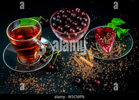 Ancora in vita con una tazza di tè forte, ciliegie mature e torta di ciliegie su uno sfondo nero. Foto Stock