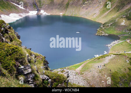 Vista incorniciata dell'occhio lago, uno dei sette laghi di Rila, tanti gli escursionisti di montagna e bella luce morbida su un altopiano roccioso Foto Stock