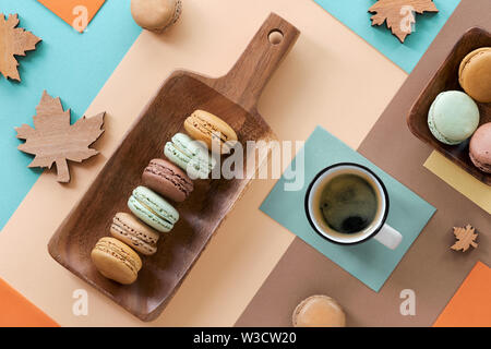 Macarons e expresso, piatto adagiare sulla carta geometrica sfondo in colori pastello con decorazioni di autunno Foto Stock