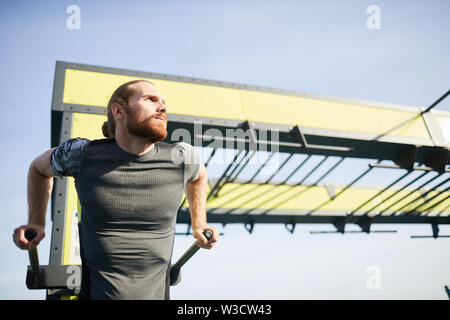 Grave pensieroso libero giovane uomo barbuto in stretto tshirt facendo pull-ups sulla barra mentre la pratica di esercizio di resistenza Foto Stock