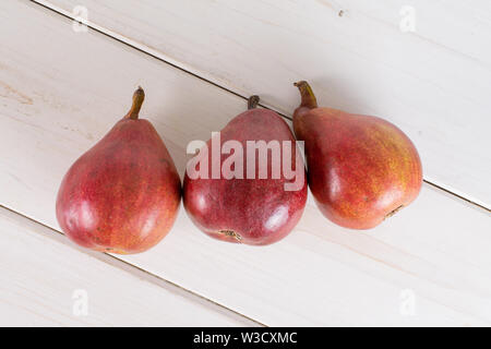 Gruppo di tre intere fresche lucido rosso scuro pera anjou flatlay su legno bianco Foto Stock