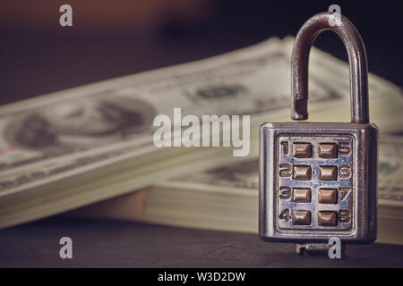 Lucchetto a combinazione e dollar banconota nelle tenebre. Concetto di segreti aziendali o di sicurezza finanziaria. Foto Stock