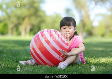 Poco ragazza asiatica posano con sfera rossa in posizione di parcheggio Foto Stock